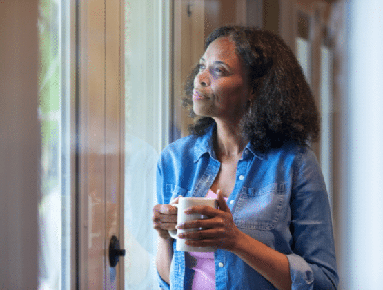 A person holding a cup looking out a window