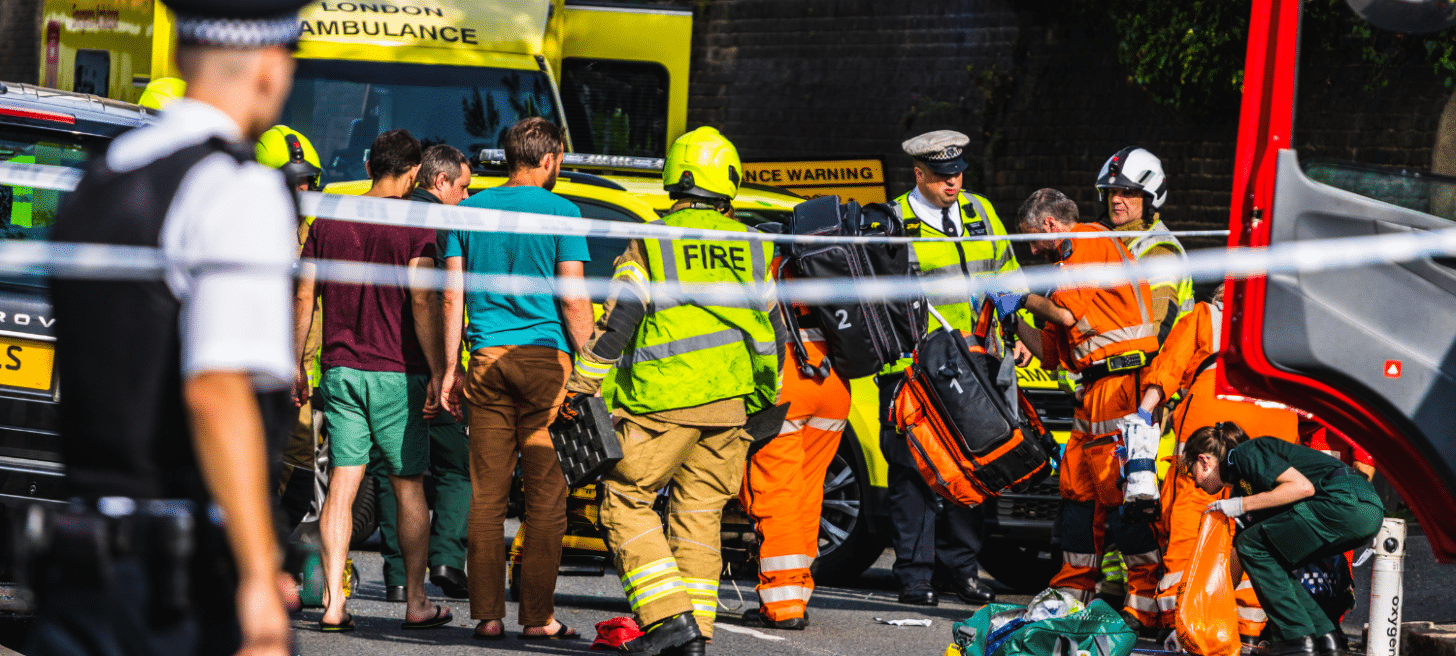 Emergency services working together at an incident on a public road - visible are ambulance crew, police and firefighters and vehicles from each.