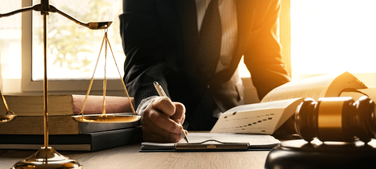 A person writing on a clipboard. There is law/court themed items on the desk where the person is writing.
