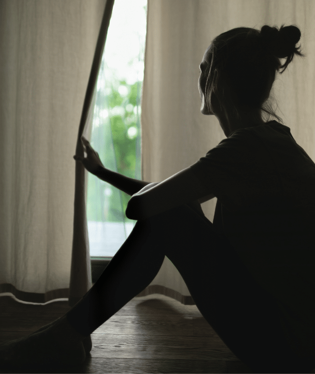 Women looking out window behind curtain at home