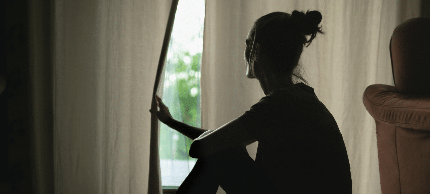 Women looking out window behind curtain at home