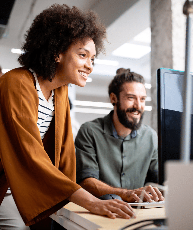 Two people looking at a computer in an office workplace.