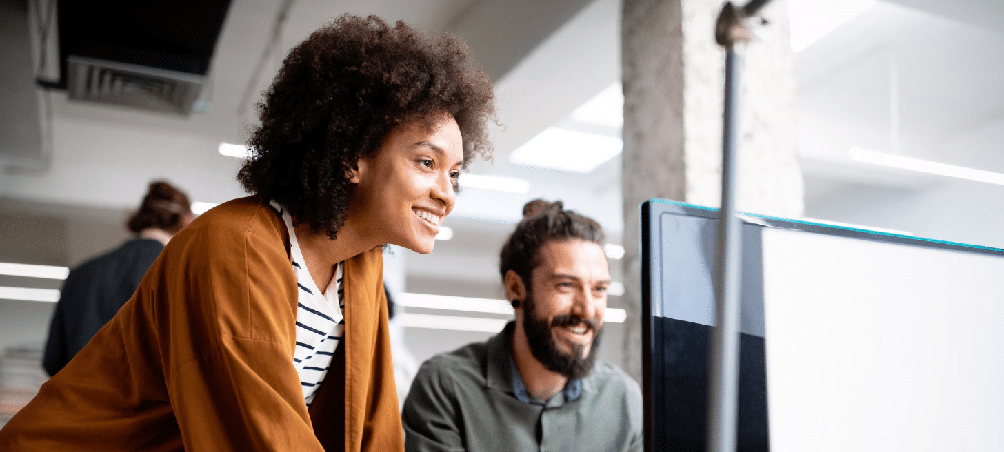 Two people looking at a computer in an office workplace.