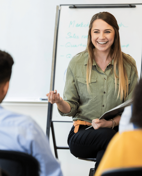 Woman leading a training session. She holds a clipboard and is sat in front of a flipchart.