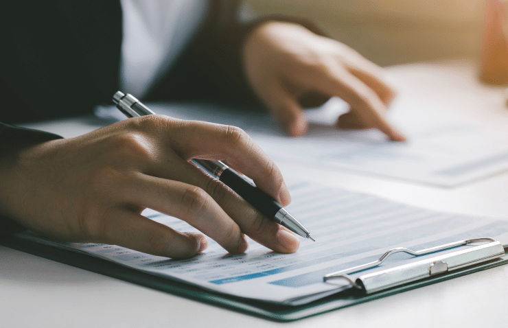 A person holding a pen to a clipboard at a table