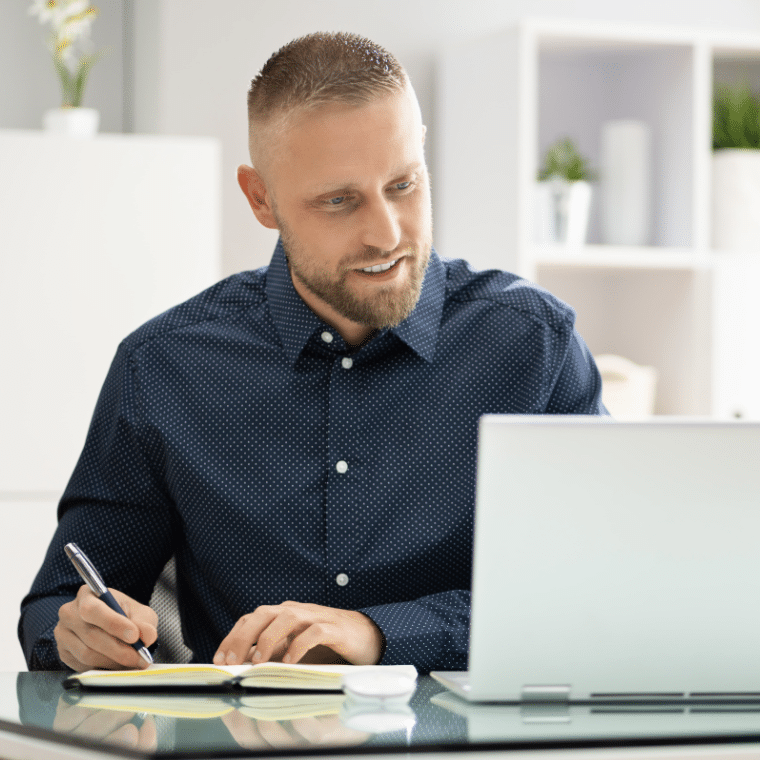Man making notes while looking at a laptop screen