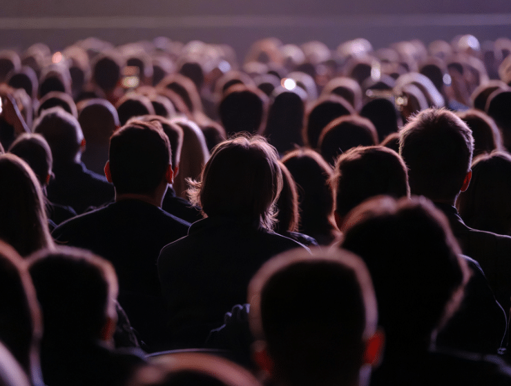 Large audience watching live performance in dimly lit venue, backs of heads visible