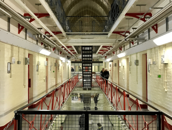 A long prison hallway with metal railings and painted brick walls.