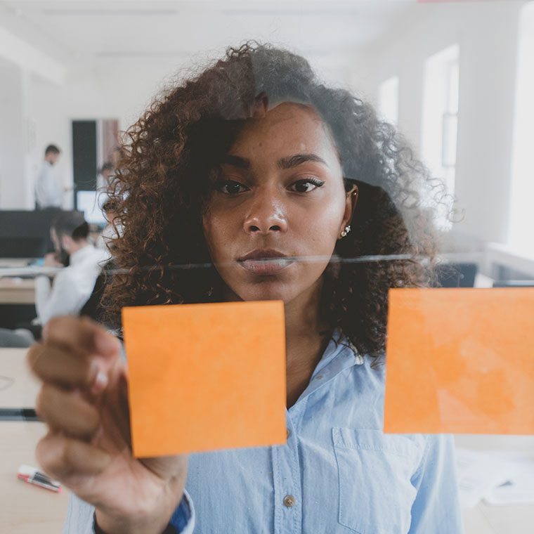 Woman in office putting post-it notes on a glass wall