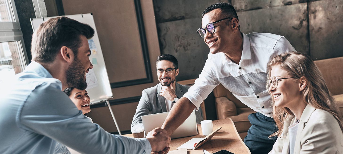 Two office workers shaking hands in front of other colleagues