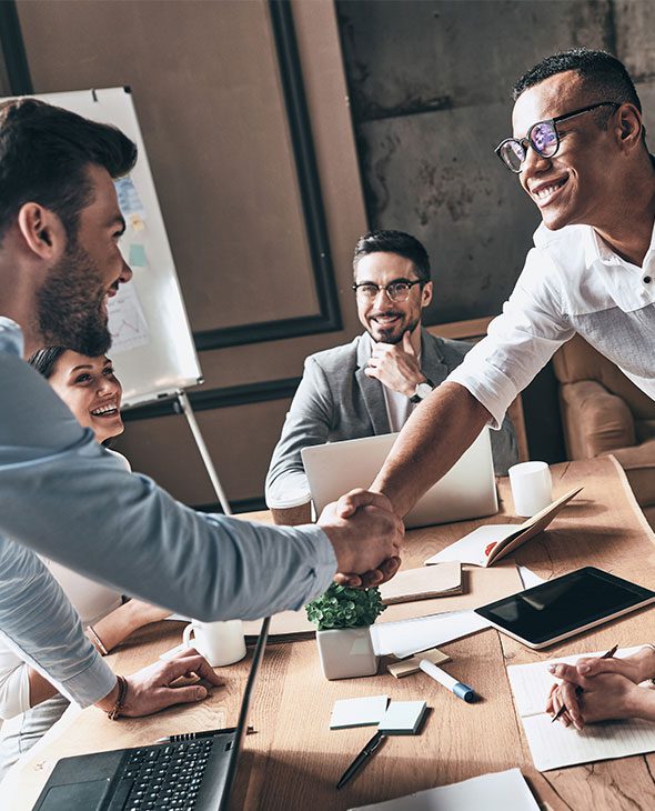 Two office workers shaking hands in front of other colleagues