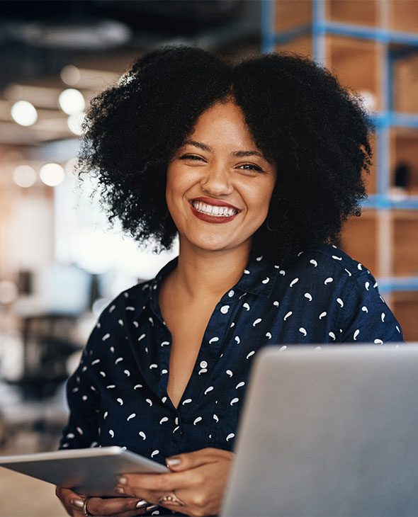 Woman working in an office on a laptop, smiling at the camera